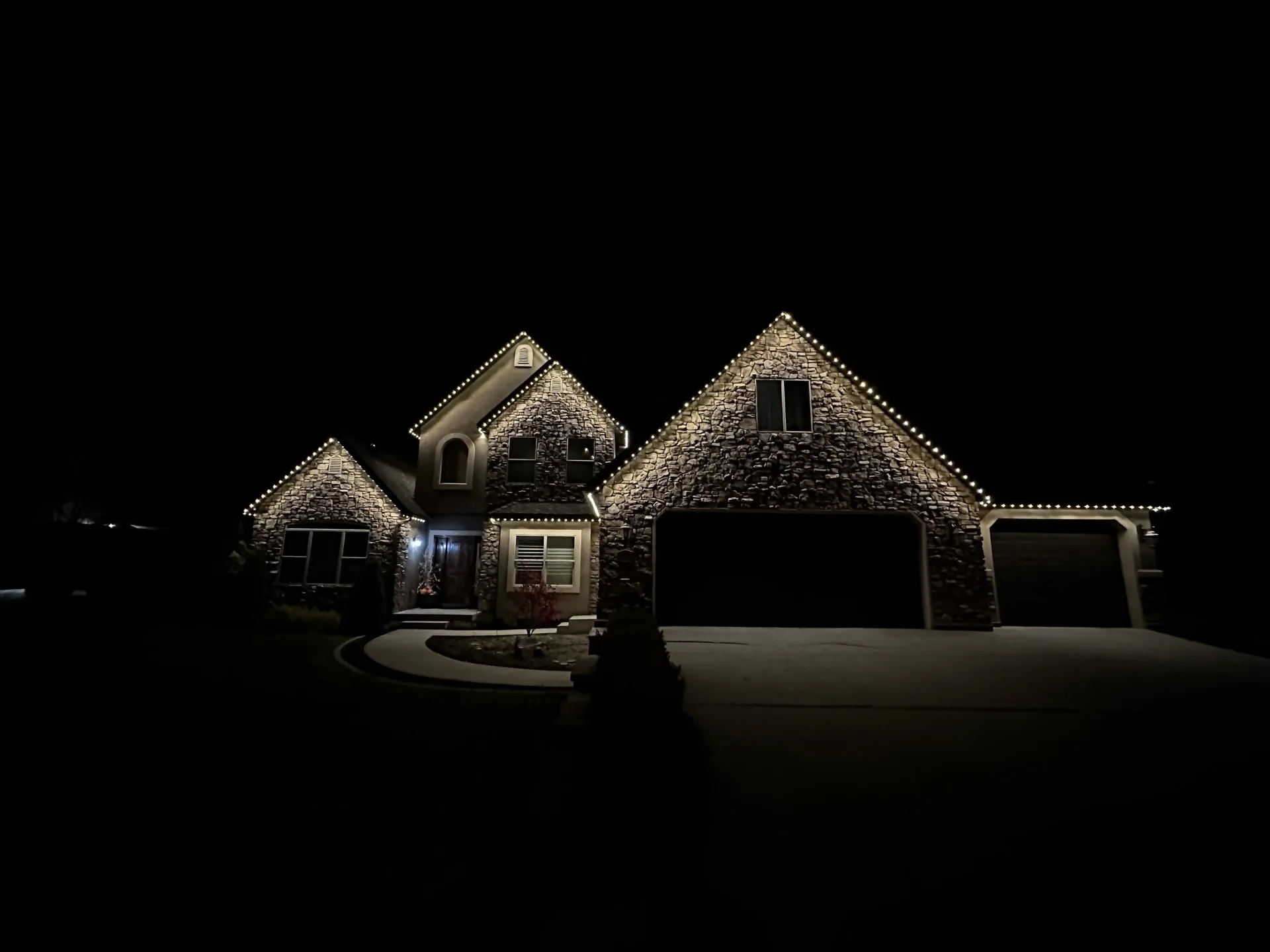 Stone home with warm white permanent lights outlining every gable