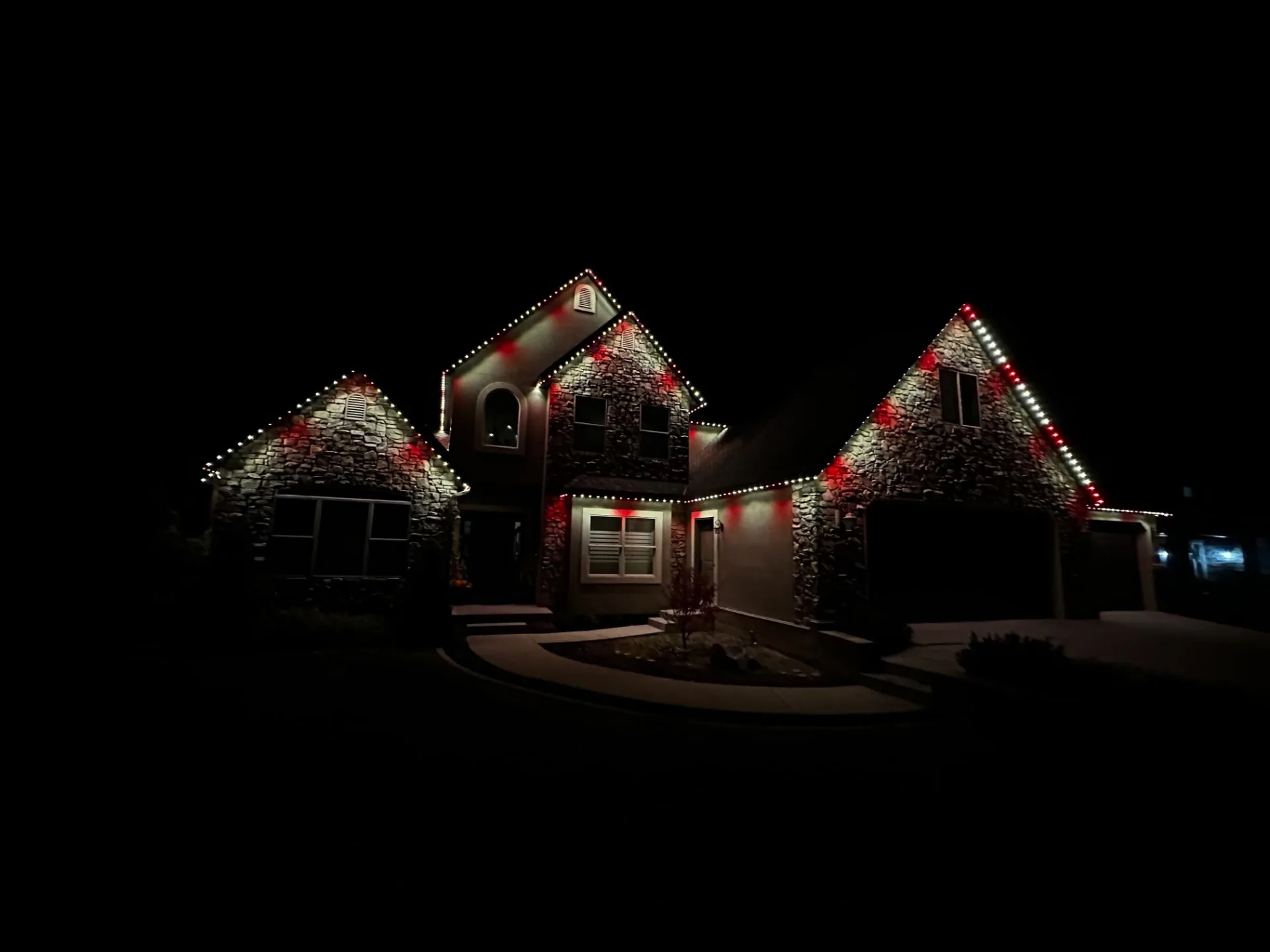 Stone home with red and white holiday lighting along the gables